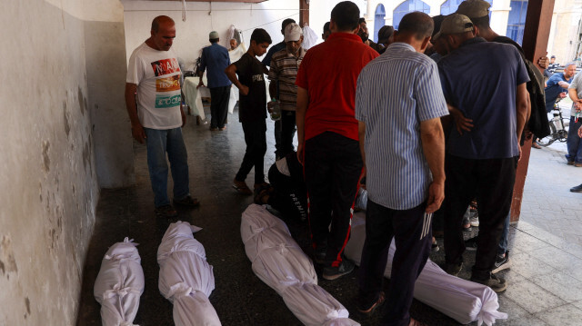 Des personnes se tenant devant les corps enveloppés des civils tués lors d'un bombardement israélien sur les écoles Hassan Salameh et Al-Nassr abritant des Palestiniens déplacés, le 4 août 2024, à l'hôpital arabe Al-Ahli, également connu sous le nom d'hôpital baptiste, dans la ville de Gaza, dans le cadre du conflit en cours entre Israël et le groupe militant du Hamas. 
