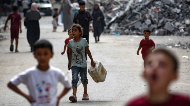 Des enfants palestiniens au milieu des débris d'habitations causés par les attaques aériennes israéliennes, se dirigent vers un point de distribution d'eau dans le camp de Bureij, dans le centre de la bande de Gaza, le 25 août 2024.