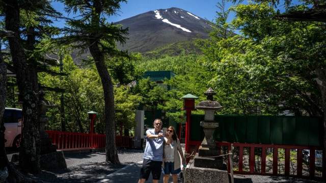 Des gens prennent des photos devant le Mont Fuji alors qu'ils visitent le sanctuaire Komitake près de la 5e station de la ligne Fuji Subaru, qui mène au populaire sentier Yoshida pour les randonneurs qui escaladent le Mont Fuji, à Narusawa, dans la préfecture de Yamanashi, le 19 juin 2024.