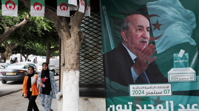 Des personnes passent devant des affiches du président algérien Abdelmajid Tebboune à l'extérieur d'un quartier général de campagne électorale à Alger le 8 septembre 2024.