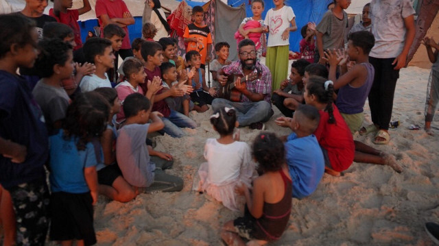 Ahmad Abu Amsha, 42 ans, enseignant de musique qui a dû fuir Beit Hanun dans le nord de la bande de Gaza, divertit des enfants sur la plage près d'un camp pour Palestiniens déplacés à Khan Younes dans le sud de la bande de Gaza, où il a trouvé refuge avec sa famille, le 1er septembre 2024. 