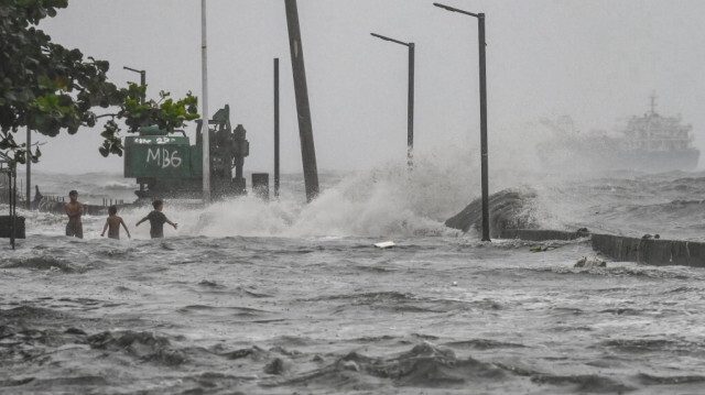 Des jeunes pataugent dans une onde de tempête le long de la baie de Manille lors de fortes pluies provoquées par la tempête tropicale Yagi, à Manille, le 2 septembre 2024.