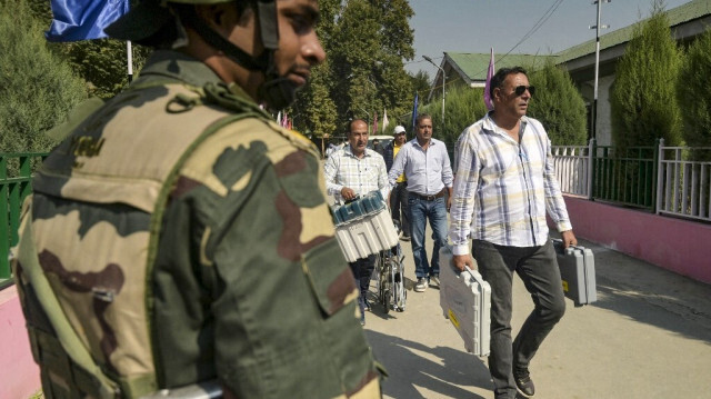 Un membre du personnel de sécurité monte la garde alors que les responsables du scrutin transportent des machines à voter électroniques (EVM), dans un centre de distribution à Srinagar le 24 septembre 2024, à la veille de la deuxième phase du scrutin lors des élections législatives.