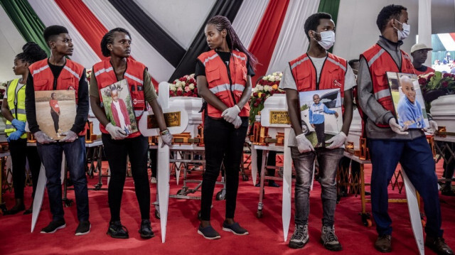 Des membres de la Croix-Rouge kenyane tiennent des portraits d'élèves à côté de leurs cercueils lors de la cérémonie de commémoration des 21 victimes de l'incendie de l'école Hillside Endarasha Academy à Mweiga, le 26 septembre 2024.