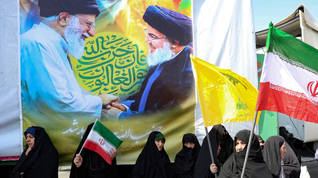 Une bannière portant une photo du guide suprême iranien, l'ayatollah Ali Khamenei (à gauche), et du chef du Hezbollah libanais, Hasan Nasrallah, est accrochée à un mur, tandis que des femmes iraniennes agitent des drapeaux nationaux lors d'une manifestation anti-israélienne à Téhéran, le 27 septembre 2024. Face à l'escalade de la violence entre Israël et le Hezbollah, l'Iran marche sur la corde raide en soutenant le Hezbollah sans se laisser entraîner dans un conflit à part entière.