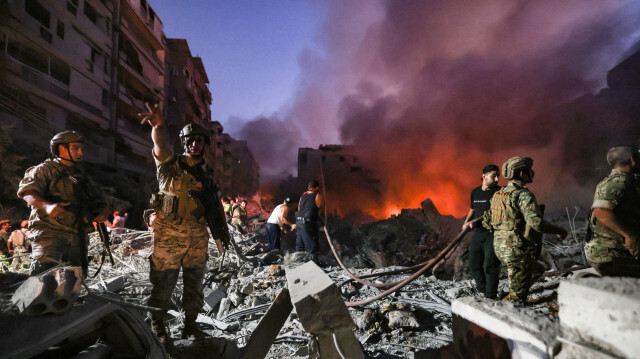 Des soldats de l'armée libanaise se rassemblent au-dessus des décombres d'un bâtiment rasé, alors que des personnes fuient les flammes, suite aux frappes aériennes israéliennes dans le quartier de Haret Hreik, dans la banlieue sud de Beyrouth, le 27 septembre 2024. Une source proche du Hezbollah a déclaré que les frappes israéliennes massives sur la banlieue sud de Beyrouth ont rasé six bâtiments.