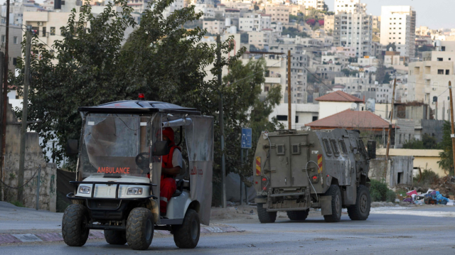 Un ambulancier palestinien conduit un buggy servant d'ambulance devant un véhicule militaire lors d'un raid israélien dans le camp de réfugiés de Nur Shams près de Tulkarem, le 2 septembre 2024.