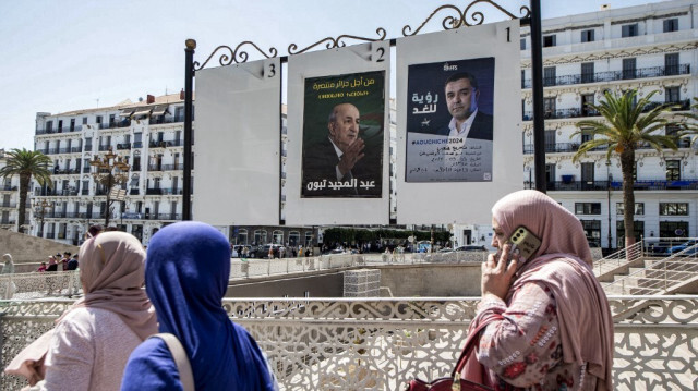 Des femmes passent devant un panneau d'affichage présentant les affiches des candidats à l'élection présidentielle, le président sortant et indépendant Abdelmajid Tebboune (à gauche) et le candidat du Front des forces socialistes Youcef Aouchiche, dans le centre d'Alger, le 5 septembre 2024.