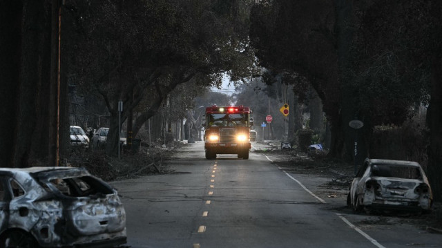 Un camion de pompiers remonte une rue où se trouvent des véhicules carbonisés par l'incendie d'Eaton à Altadena, en Californie, le 10 janvier 2025.