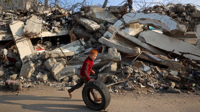 Un garçon joue avec un pneu à côté des décombres des bâtiments détruits par une attaque aérienne israélienne près du camp de réfugiés de Nuseirat, dans le centre de la bande de Gaza, le 11 janvier 2025.