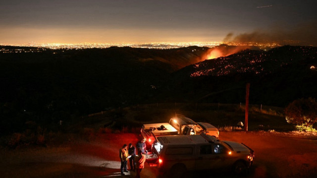 L'horizon du centre-ville de Los Angeles est visible au loin alors que les pompiers surveillent l'incendie de Palisades près du quartier de Mandeville Canyon et d'Encino, en Californie, le 11 janvier 2025. 