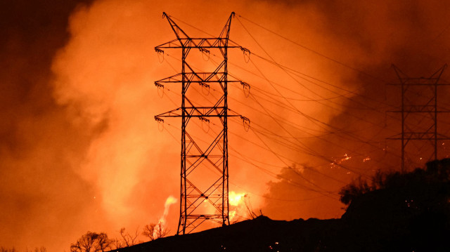 Des flammes et de la fumée sont visibles près des lignes électriques alors que l'incendie des Palisades se développe près du quartier de Mandeville Canyon et d'Encino, en Californie, le 11 janvier 2025. L'incendie de Palisades, le plus important des incendies de Los Angeles, s'est propagé vers des quartiers jusque-là épargnés le 11 janvier, obligeant à de nouvelles évacuations et réduisant les espoirs de maîtrise de la catastrophe. Dans toute la ville, au moins 16 personnes ont trouvé la mort dans les multiples incendies qui ont ravagé des zones résidentielles depuis le 7 janvier, rasant des milliers d'habitations dans une destruction que le président américain Joe Biden a comparée à une "scène de guerre".