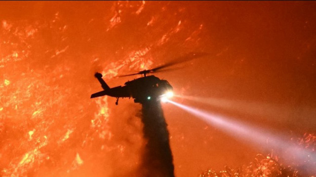 Un hélicoptère de lutte contre les incendies largue de l'eau alors que l'incendie de Palisades progresse près des quartiers de Mandeville Canyon et Encino, en Californie, le 11 janvier 2025.