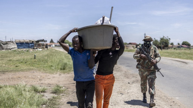 Des mineurs informels présumés, communément appelés "zama zamas" ("ceux qui essaient" en langue zouloue), portent des objets confisqués lors de l'opération Shanela dans le quartier informel de Soul City près de Kagiso, le 14 décembre 2023. 