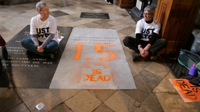 Deux militantes assises au sol à côté de la tombe de Charles Darwin, après y avoir inscrit "1.5 is dead" en protestation contre l'inaction face au changement climatique, à l'intérieur de l'abbaye de Westminster, au centre de Londres, le 13 janvier 2015.