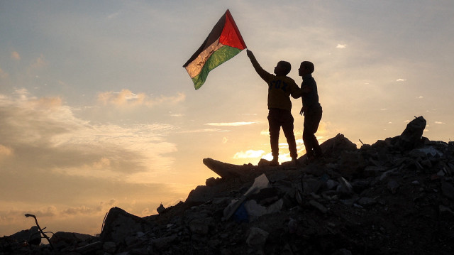 Un garçon court avec un drapeau palestinien sur un monticule de décombres dans un camp pour personnes déplacées par le conflit à Bureij, dans le centre de la bande de Gaza, le 17 janvier 2025, suite à l'annonce d'une trêve dans le cadre de la guerre entre Israël et le Hamas.