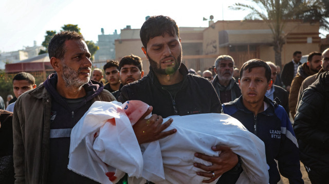 Un parent porte le corps d'un enfant, l'un des quatre membres de la famille palestinienne al-Qadra (les parents et leurs deux enfants) tués lors d'une frappe israélienne qui a touché leur tente au nord de Khan Yunis dans le sud de la bande de Gaza, dans la cour de l'hôpital Nasser le 18 janvier 2025, un jour avant la mise en œuvre prévue d'un accord de cessez-le-feu entre Israël et le Hamas.