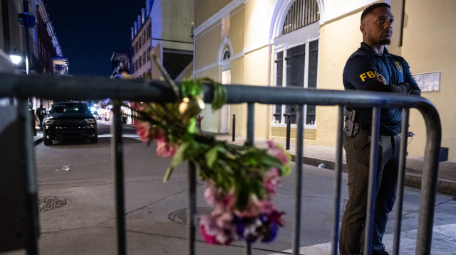 Un membre du FBI, derrière un bouquet de fleurs attaché à une clôture, à un pâté de maisons de Bourbon Street, lieu de l'attaque à la voiture bélier ayant eu lieu plus tôt le matin du 1er janvier 2025 à la Nouvelle-Orléans, en Louisiane.