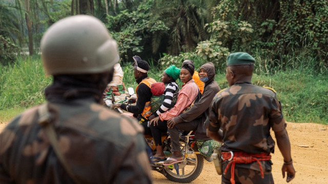 Des civils sur une moto-taxi croisent le chemin des soldats du 21e bataillon DP des Forces armées de la RDC (FARDC) sur la route entre Beni et Bulongo, au Nord-Kivu, dans l'est de la République démocratique du Congo, le 17 décembre 2024.