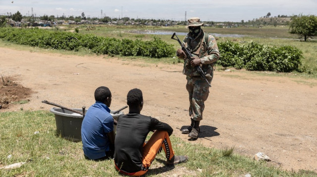 Un soldat de la South African National Defence Force (SANDF) se tient à côté de mineurs informels présumés, communément appelés "zama zamas" ("ceux qui essaient" en langue zouloue), lors de l'opération "Shanela" dans le quartier informel de Soul City, près de Kagiso, le 14 décembre 2024. 