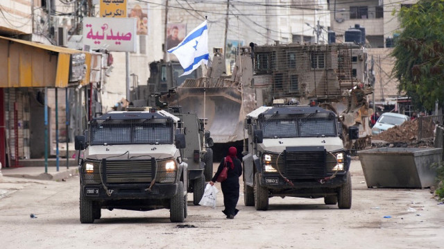 Une femme palestinienne passe devant des véhicules de l'armée d'occupation israélienne lors d'un raid militaire à Jénine, en Palestine occupée, le 22 janvier 2025.