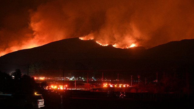 Des camions de pompiers et des véhicules de sécurité publique sont visibles au premier plan tandis que des flammes rougeoyantes et de la fumée s'élèvent de l'incendie Hughes à Castaic, dans le nord-ouest du comté de Los Angeles, en Californie, le 22 janvier 2025