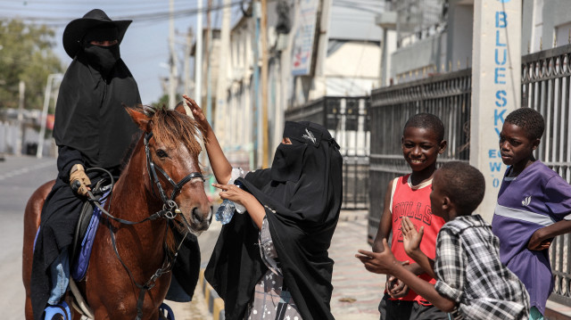 Shukri Osman Muse (à gauche), la première femme cavalière de Mogadiscio, monte son cheval tandis qu'un groupe d'enfants caresse curieusement l'animal, à Mogadiscio, le 17 janvier 2025.