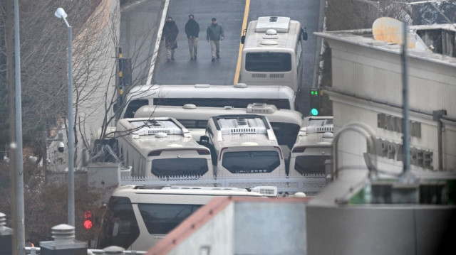 Le personnel de sécurité marche sur la route avec des bus bloquant une porte d'entrée pour protéger le président sud-coréen Yoon Suk Yeol d'une éventuelle seconde tentative d'arrestation par le Bureau d'enquête sur la corruption pour les hauts fonctionnaires dans l'enceinte de la résidence présidentielle, vue d'une colline à Séoul, le 6 janvier 2025. 