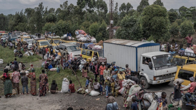 Des personnes se rassemblent sur une route fréquentée tout en transportant certains de leurs biens alors qu'elles fuient le territoire de Masisi suite aux affrontements entre les rebelles du M23 et les forces gouvernementales, sur une route près de Sake.