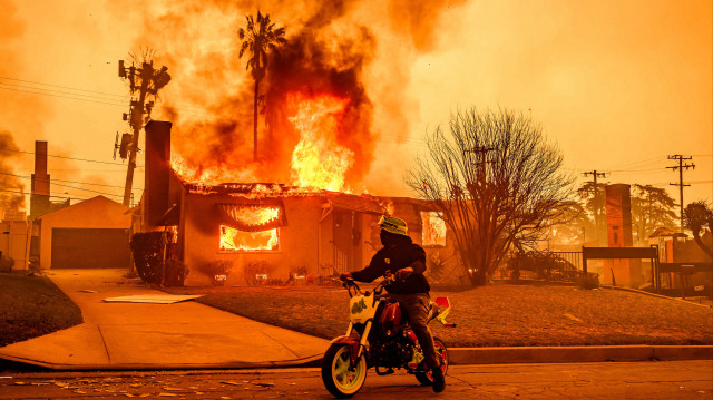 Un motocycliste s'arrête pour regarder une maison en flammes lors de l'incendie d'Eaton dans la région d'Altadena, dans le comté de Los Angeles, en Californie, le 8 janvier 2025. 