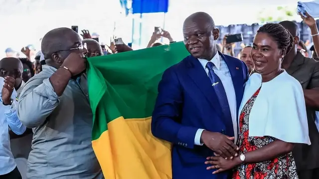 Le chef de la junte gabonaise, Brice Oligui Nguema (2e à droite), est drapé d'un drapeau gabonais, debout à côté de son épouse Zita Nyangue Oligui Nguema (à droite), alors qu'ils célèbrent sa victoire à l'élection présidentielle, à son quartier général de campagne électorale à Libreville, le 13 avril 2025.