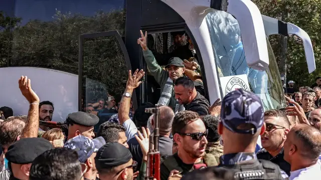 L'un des prisonniers palestiniens, libéré dans le cadre d'un échange de prisonniers contre des otages et d'un accord de cessez-le-feu entre Israël et le Hamas, fait un geste alors que lui et d'autres descendent de leur bus à leur arrivée au Centre culturel de Ramallah, à Ramallah, en Palestine occupée, le 13 octobre 2025, en provenance de la prison militaire d'Ofer dans les territoires palestiniens occupés par Israël.