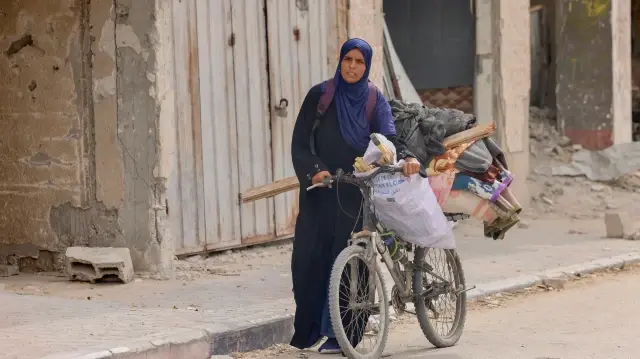 Une femme pousse un vélo chargé de ses affaires à travers les décombres à Khan Yunis, dans le sud de Gaza, le 12 octobre 2025, alors que les familles reviennent pour récupérer leurs biens et évaluer les dégâts après le retrait progressif d'Israël.