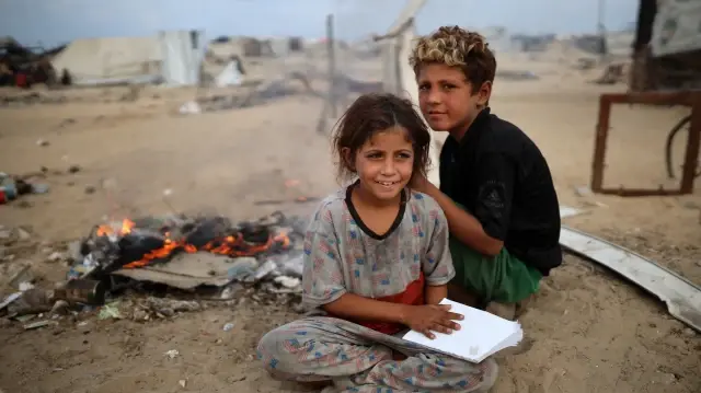 Des enfants palestiniens déplacés sont assis devant leur tente dans un camp de déplacés près du port de Gaza, le 19 octobre 2025.