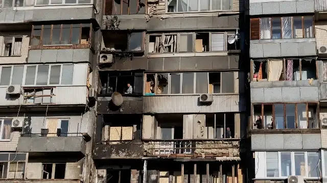 Des habitants nettoient les débris de verre provenant de leurs fenêtres brisées à la suite d'une attaque de drones à Kiev, le 26 octobre 2025, dans le contexte de l'invasion russe en Ukraine.