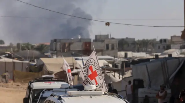 De la fumée s'élève à l'arrière-plan alors que des véhicules du Comité international de la Croix-Rouge (CICR) traversent Khan Yunis, dans le sud de la bande de Gaza, le 26 octobre 2025.