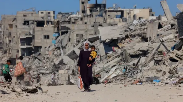Une femme marche parmi les décombres en portant un enfant dans le nord de la bande de Gaza, le 16 octobre 2025.