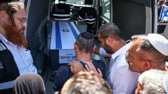 Des personnes en deuil touchent le cercueil placé à l'arrière d'une camionnette alors qu'elles font leurs adieux lors du cortège funèbre de Yossi Sharabi, dans la ville israélienne centrale de Rishon Letzion, le 27 octobre 2025.