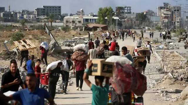 Des Palestiniens portant des sacs reviennent d'un point de distribution alimentaire géré par le groupe Gaza Humanitarian Foundation (GHF), soutenu par les États-Unis et Israël, près du corridor de Netsarim, dans le centre de la bande de Gaza, le 5 octobre 2025.