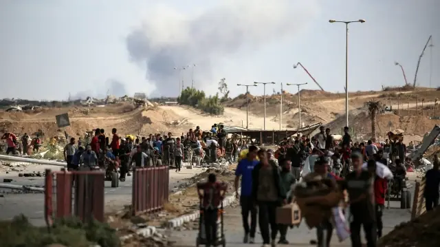 Une colonne de fumée s'élève à l'arrière-plan alors que des Palestiniens reviennent d'un point de distribution alimentaire géré par le groupe Gaza Humanitarian Foundation (GHF), soutenu par les États-Unis et Israël, près du corridor de Netsarim, dans le centre de la bande de Gaza, le 5 octobre 2025.