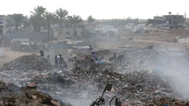 Des enfants palestiniens déplacés cherchent des objets pouvant servir de combustible pour cuisiner parmi un tas d'ordures en feu dans le camp de réfugiés de Bureij, dans le centre de la bande de Gaza, le 6 octobre 2025.