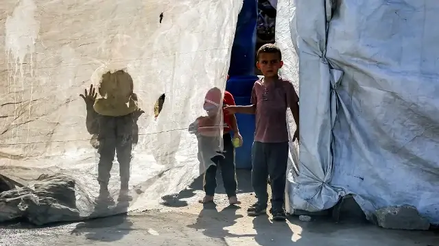 Des enfants se tiennent derrière une toile à l'extérieur d'une tente dans un camp pour personnes déplacées par la guerre, dans le nord de Nuseirat, dans le centre de la bande de Gaza, le 7 octobre 2025.