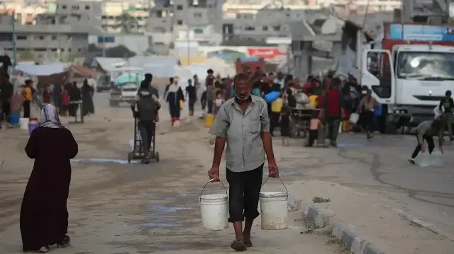 Un Palestinien déplacé transporte deux seaux remplis d'eau potable provenant d'une citerne mobile dans le camp de réfugiés de Bureij, dans le centre de la bande de Gaza, le 6 octobre 2025. 