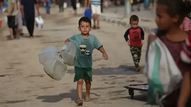 Un enfant palestinien déplacé porte des jerrycans vides alors que les gens se dirigent vers des citernes mobiles pour s'approvisionner en eau potable dans le camp de réfugiés de Bureij, dans le centre de la bande de Gaza, le 6 octobre 2025.