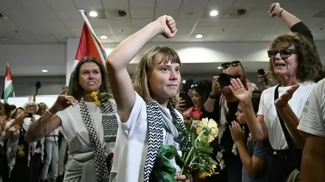La militante suédoise pour le climat Greta Thunberg lève le poing à son arrivée, aux côtés d'activistes qui naviguaient à bord de navires de la flottille d'aide humanitaire à destination de Gaza avant d'être arrêtés et détenus par les forces israéliennes, accueillis par une foule de sympathisants, dans la zone des arrivées de l'aéroport international d'Athènes, le 6 octobre 2025.