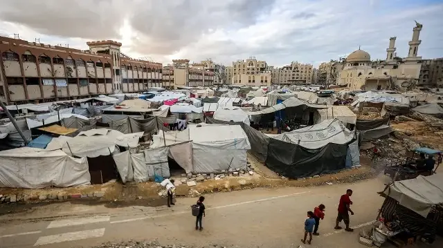 Un homme et des enfants passent devant des tentes abritant des personnes déplacées par la guerre, installées près de la mosquée Sheikh Hamad bin Khalifa Al-Thani, fortement endommagée, dans le complexe résidentiel Hamad City construit par le Qatar au nord-ouest de Khan Yunis, dans le sud de la bande de Gaza, le 6 octobre 2025.
