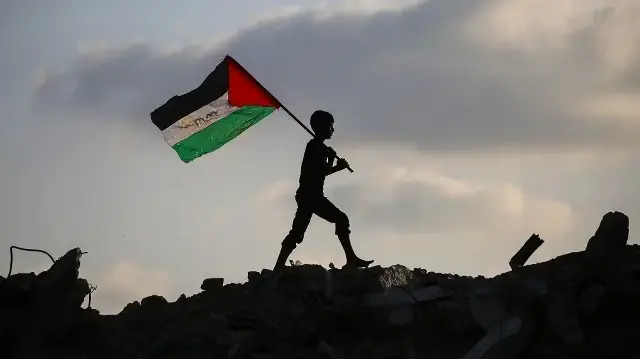 Un enfant palestinien déplacé agite un drapeau national palestinien alors qu'il marche sur les décombres d'un bâtiment détruit dans le camp de réfugiés de Bureij, dans le centre de la bande de Gaza, le 22 septembre 2025.