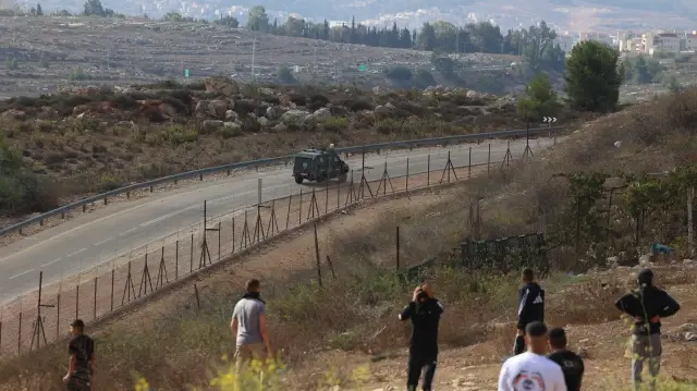 Des jeunes Palestiniens regardent un véhicule blindé des forces israéliennes patrouiller la route à l'extérieur de la prison militaire d'Ofer, située entre Ramallah et Beitunia, en Cisjordanie occupée, le 13 octobre 2025.
