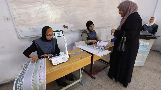 Des agents électoraux vérifient l'identité d'un électeur dans un bureau de vote du quartier de Salhiya à Bagdad, le 11 novembre 2025, lors des élections législatives irakiennes.