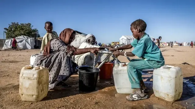 Des réfugiés soudanais remplissent des récipients d'eau à un point d'eau dans le camp de transit de Tine au Tchad, le 10 novembre 2025.